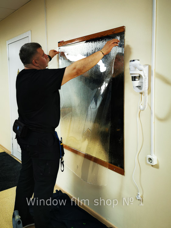 Installer applying clear safety film to an interior window with a squeegee