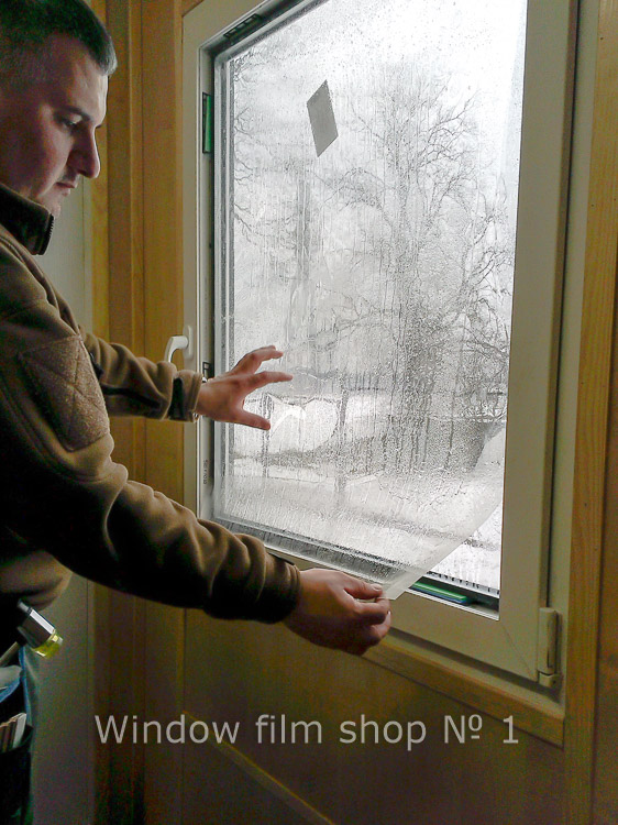 Installer pressing clear security film onto a window from the inside, winter outside
