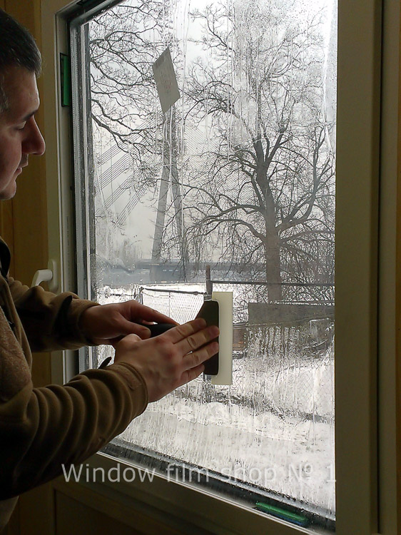Installer pressing clear protective film onto a window from the inside, winter outside