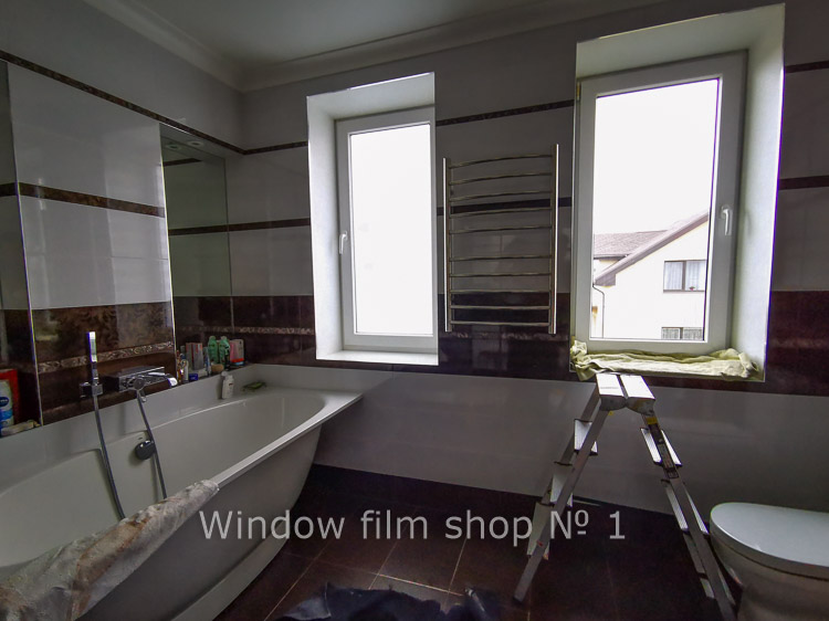 Bathroom with two windows: the left one covered with white matte film, the right one clear with the neighbouring houses visible
