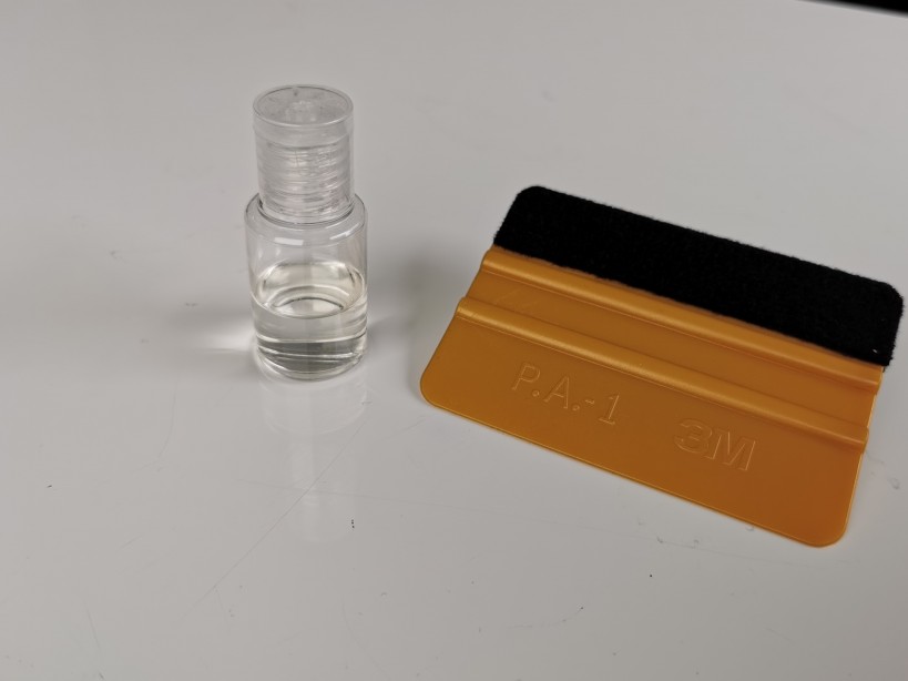 Gold 3M squeegee with a black felt edge next to a bottle of mounting solution