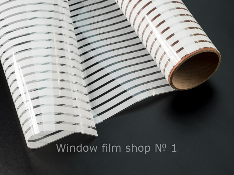 Roll of clear window film with white matte stripes, partly unrolled